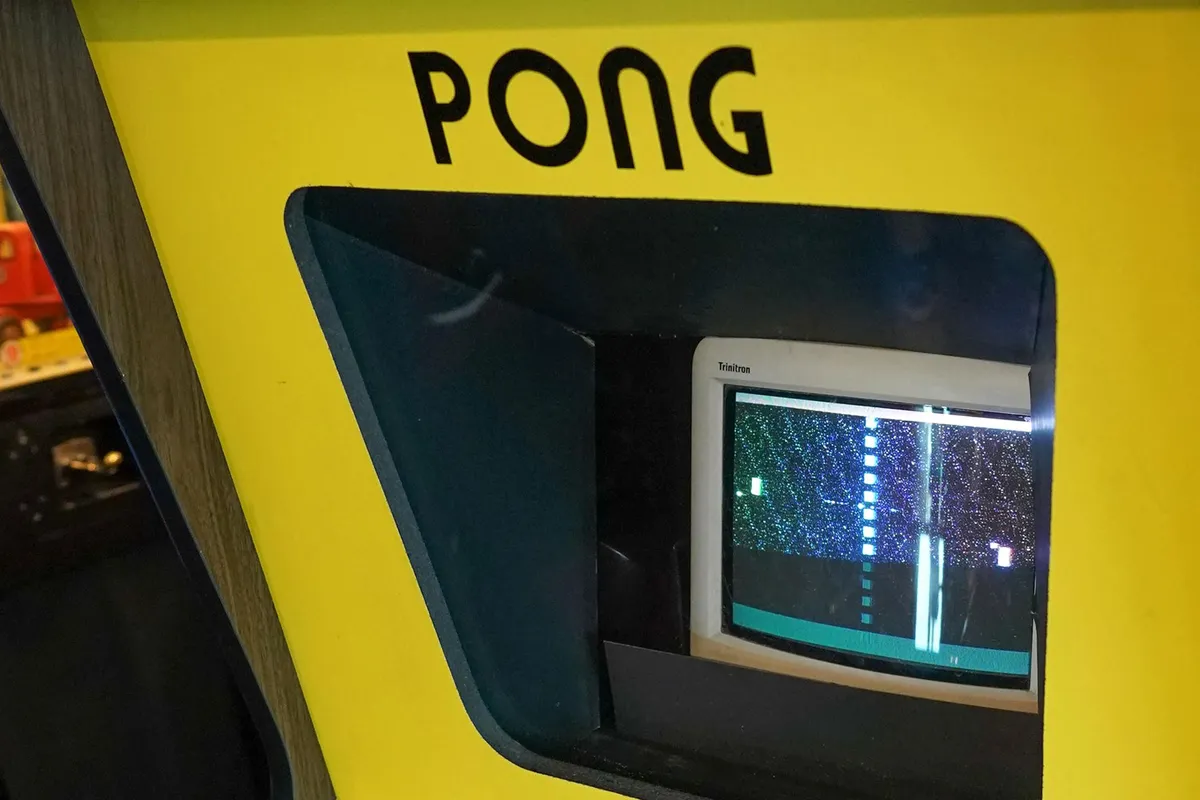 Pong arcade game in yellow cabinet containing black and white TV display, two knobs are labeled Player 1 and Player 2, Atari logo visible.